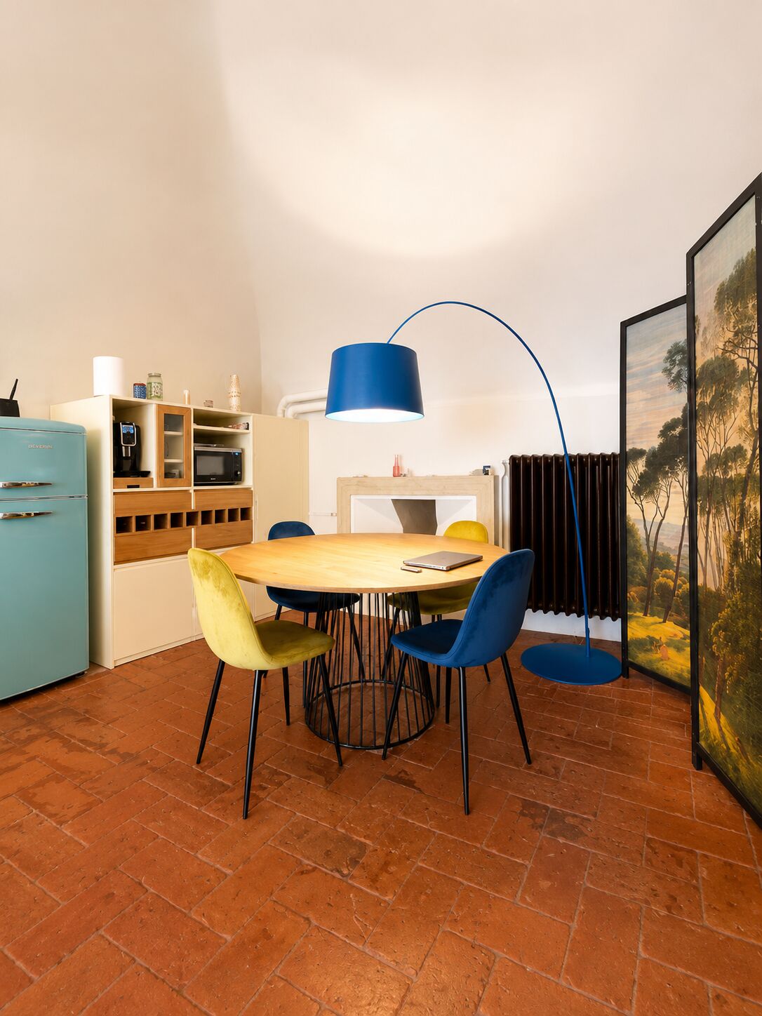 La zona pranzo con tavolo rotondo, lampada ad arco blu e paravento dipinto